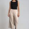 A person wearing loose, beige wide-leg pants and cream sandals, paired with an olive green top. The photo shows the lower half of their body against a plain light background. Elsewhere Fashion